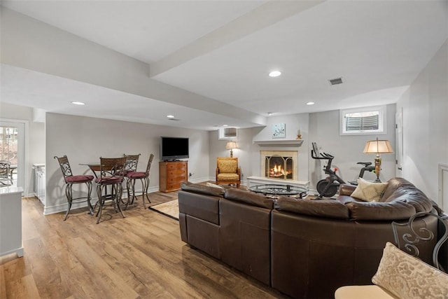 living room featuring light wood finished floors, recessed lighting, visible vents, a lit fireplace, and baseboards