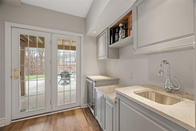 kitchen with wood finished floors, light stone counters, a sink, and gray cabinetry