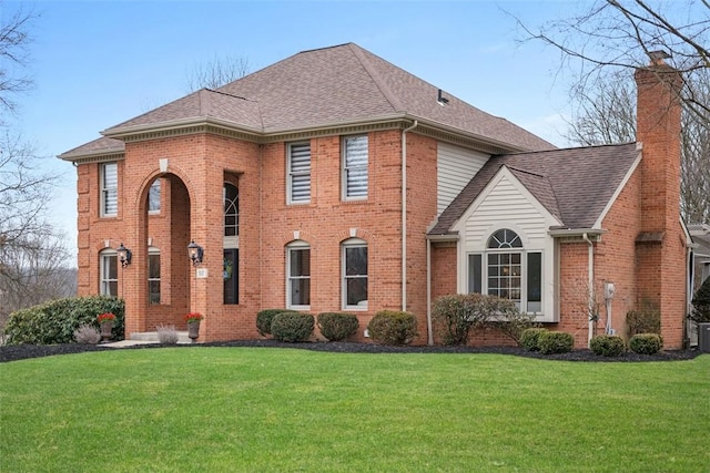 view of front of property with a shingled roof, a front yard, brick siding, and a chimney