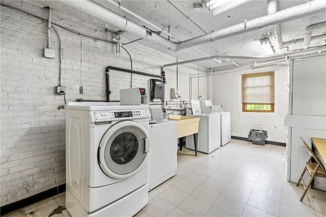 shared laundry area with light floors, independent washer and dryer, and brick wall