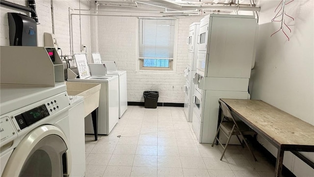 community laundry room with brick wall, stacked washer / dryer, and washing machine and dryer