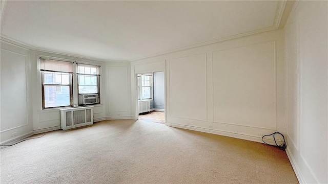 spare room with crown molding, light colored carpet, a decorative wall, and radiator heating unit