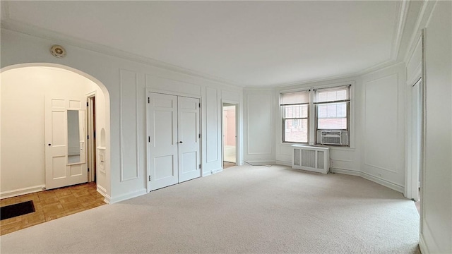 unfurnished bedroom featuring ornamental molding, arched walkways, a decorative wall, and radiator heating unit