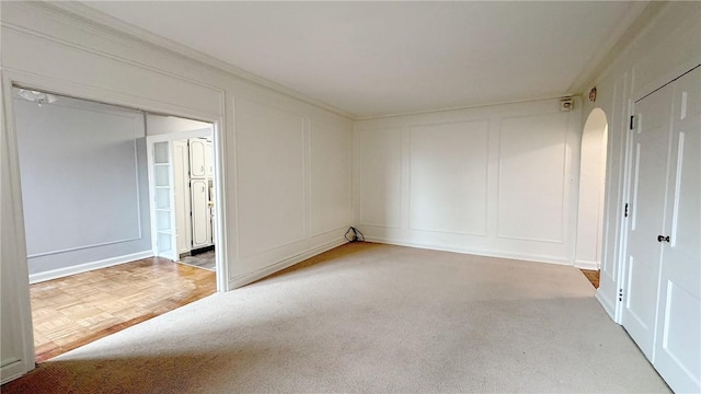 spare room with crown molding, light carpet, and a decorative wall