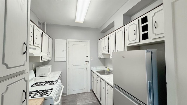 kitchen featuring white appliances, light countertops, under cabinet range hood, white cabinetry, and a sink