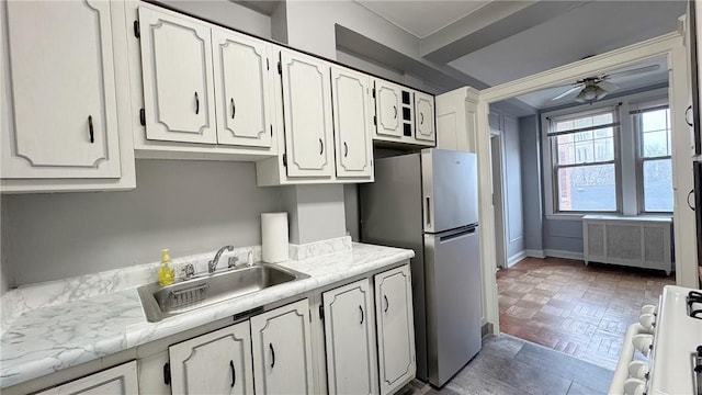 kitchen featuring a sink, white cabinetry, range with gas stovetop, freestanding refrigerator, and radiator heating unit