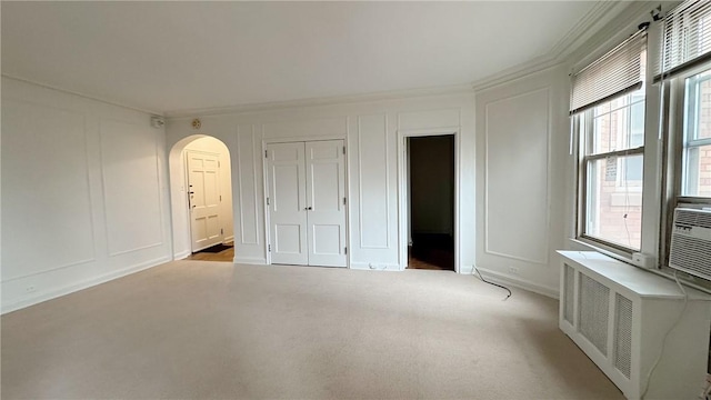 unfurnished bedroom with arched walkways, radiator heating unit, carpet floors, a decorative wall, and a closet