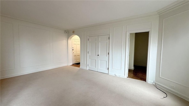 unfurnished bedroom featuring carpet floors, arched walkways, crown molding, a closet, and a decorative wall