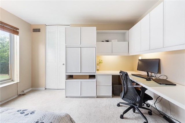 office area featuring baseboards, visible vents, built in desk, and light colored carpet