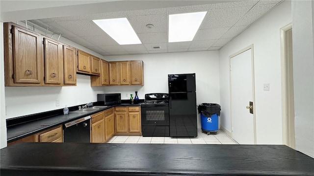 kitchen with a drop ceiling, light tile patterned flooring, a sink, black appliances, and dark countertops