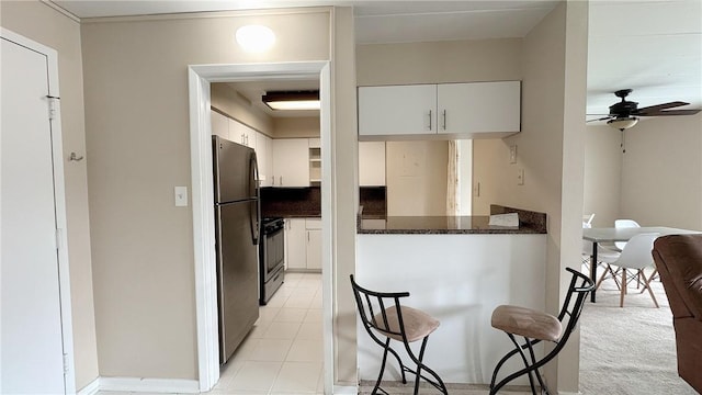 kitchen featuring a ceiling fan, freestanding refrigerator, white cabinetry, stove, and light tile patterned flooring