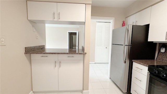 kitchen featuring dark stone countertops, freestanding refrigerator, white cabinetry, black gas stove, and light tile patterned flooring