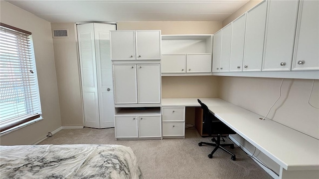 unfurnished bedroom with light colored carpet, multiple windows, built in study area, and visible vents