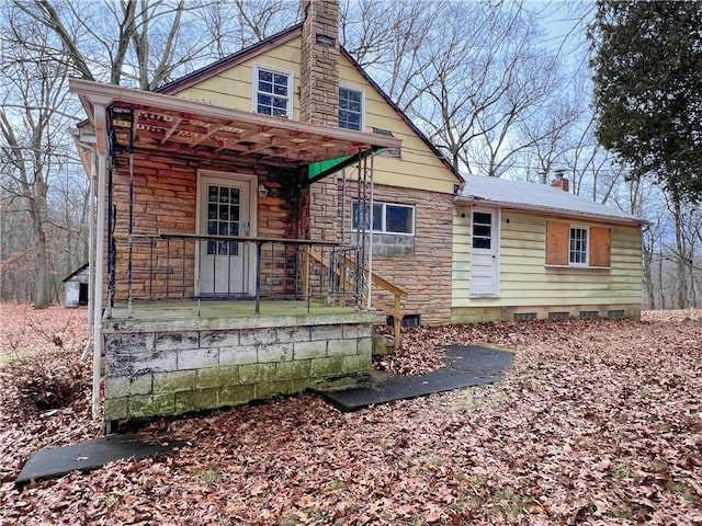 view of front facade featuring crawl space, covered porch, a chimney, and stone siding