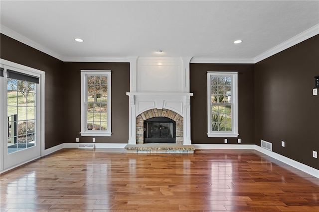 unfurnished living room with a wealth of natural light, visible vents, a stone fireplace, and wood finished floors