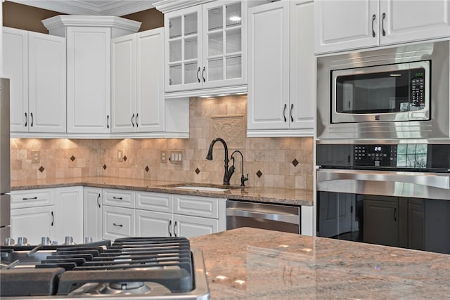 kitchen with decorative backsplash, glass insert cabinets, stainless steel appliances, white cabinetry, and a sink