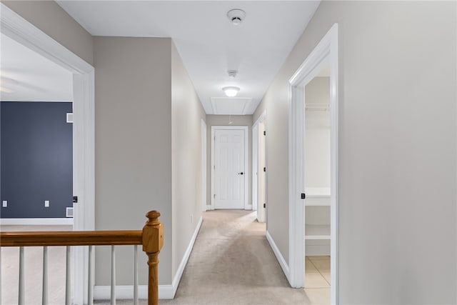 hallway with attic access, light colored carpet, and baseboards