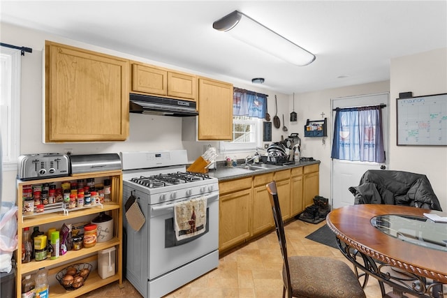 kitchen featuring light brown cabinets, under cabinet range hood, a sink, white gas range oven, and dark countertops