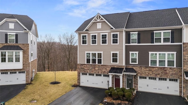 townhome / multi-family property with driveway, stone siding, roof with shingles, an attached garage, and a front yard