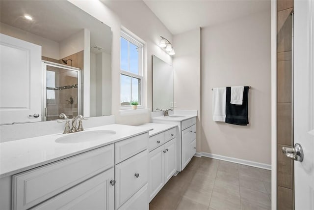 bathroom with double vanity, a shower stall, baseboards, and a sink