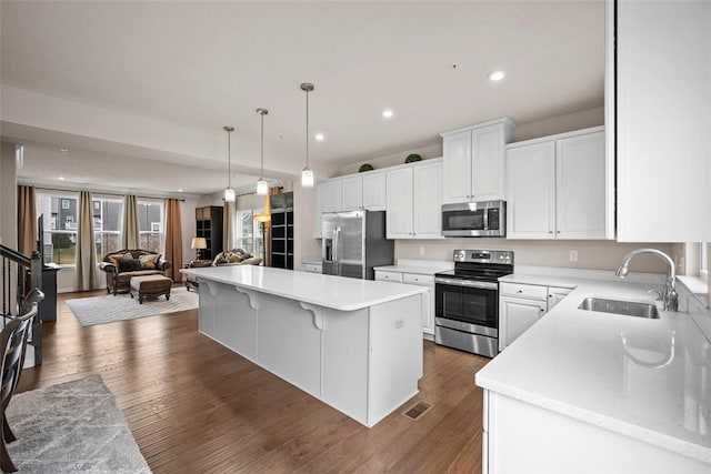 kitchen featuring dark wood finished floors, appliances with stainless steel finishes, open floor plan, white cabinetry, and a sink