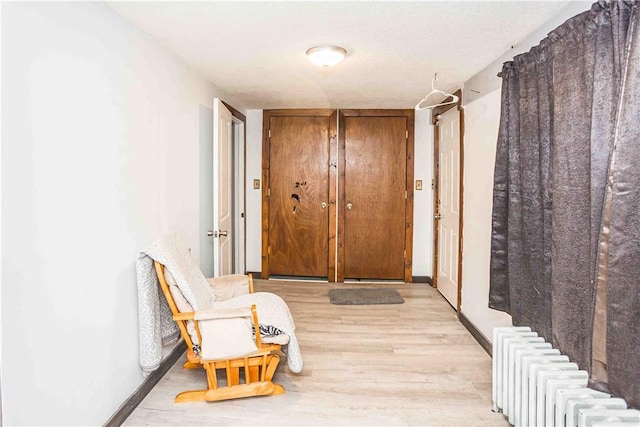 hallway with baseboards, light wood-style flooring, and radiator