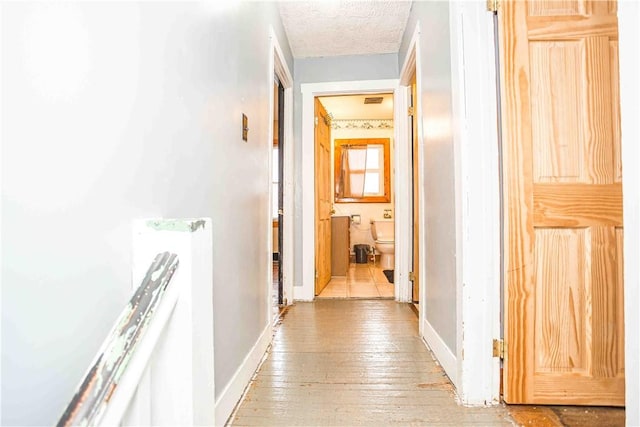 corridor with light wood finished floors, baseboards, and a textured ceiling