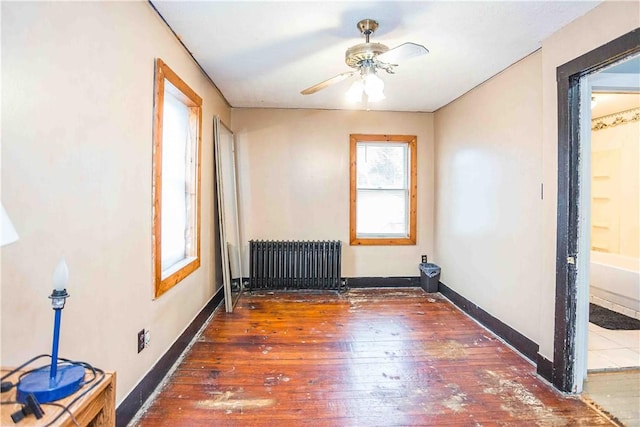 spare room with baseboards, hardwood / wood-style floors, a ceiling fan, and radiator