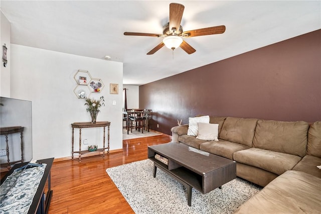 living area with light wood-style flooring, baseboards, and a ceiling fan