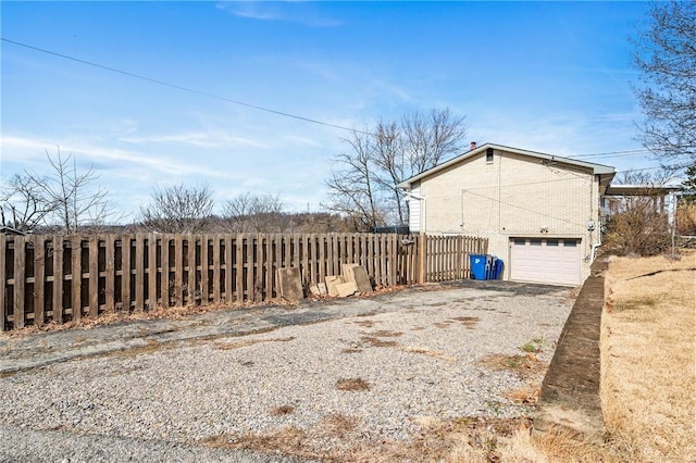 view of side of home featuring an attached garage, driveway, fence, and brick siding