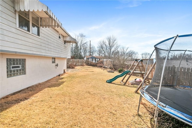 view of yard featuring a trampoline, a playground, and fence