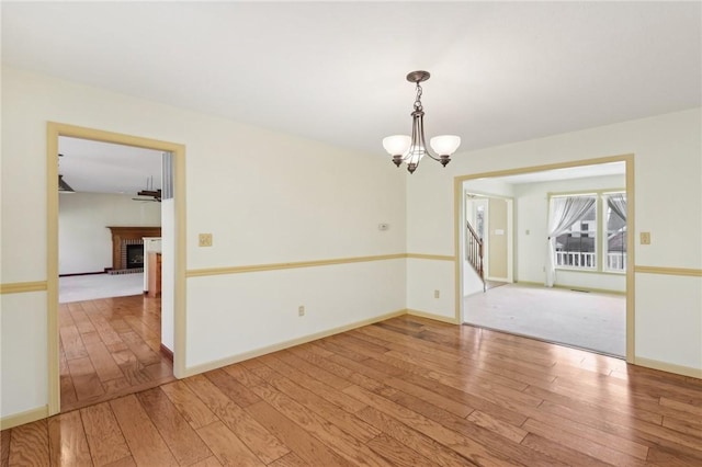 unfurnished room with an inviting chandelier, light wood-style flooring, a fireplace, and baseboards