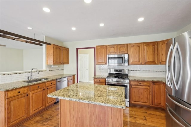 kitchen with stainless steel appliances, a sink, hardwood / wood-style floors, and a kitchen island