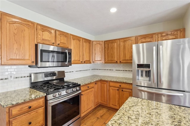 kitchen featuring light stone counters, light wood finished floors, stainless steel appliances, decorative backsplash, and brown cabinetry