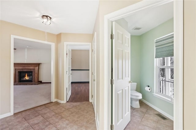 bathroom featuring a brick fireplace, baseboards, visible vents, and toilet