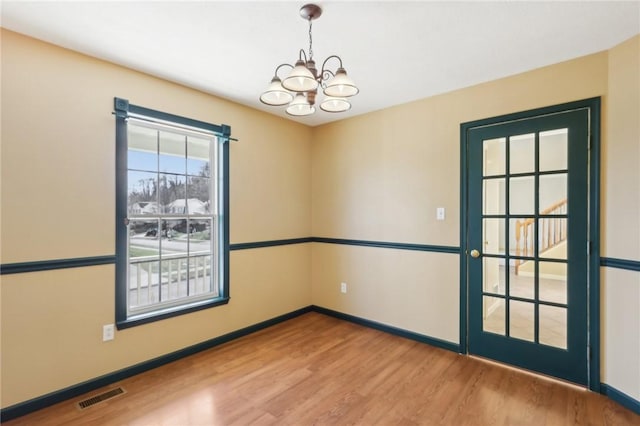 spare room with an inviting chandelier, baseboards, visible vents, and wood finished floors