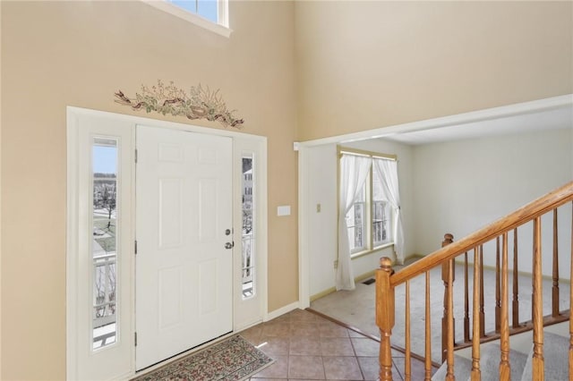 foyer entrance featuring baseboards, stairway, a high ceiling, and tile patterned floors