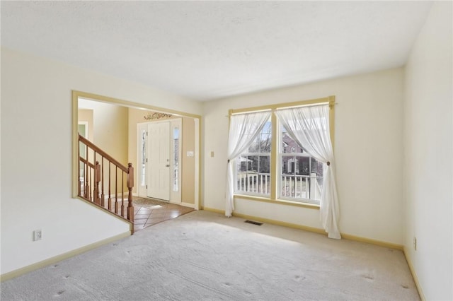 carpeted foyer with baseboards, visible vents, and stairway