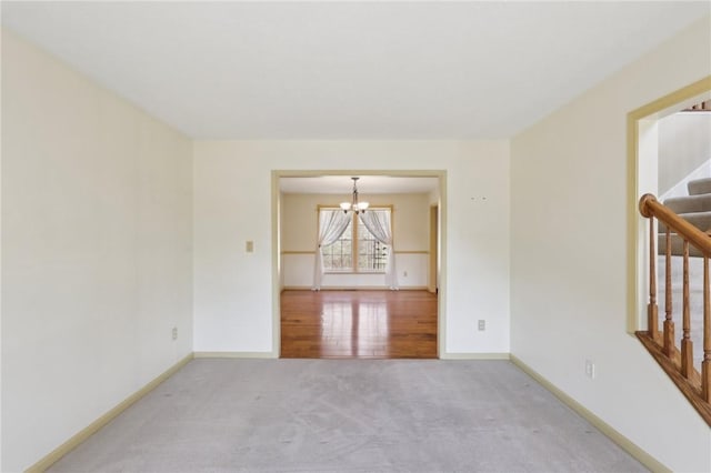 carpeted empty room with an inviting chandelier, baseboards, and stairway