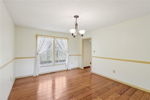 unfurnished dining area featuring wood-type flooring, visible vents, baseboards, and an inviting chandelier