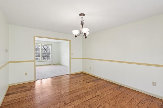 spare room featuring a chandelier, baseboards, and wood finished floors