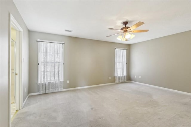 carpeted spare room with ceiling fan, a wealth of natural light, visible vents, and baseboards