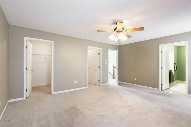 unfurnished bedroom featuring light carpet, a spacious closet, baseboards, and a ceiling fan