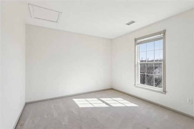 carpeted empty room with attic access, visible vents, and baseboards