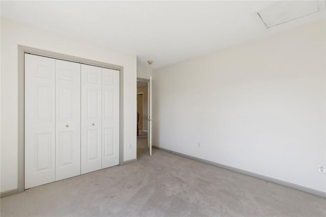 unfurnished bedroom featuring carpet floors, a closet, attic access, and baseboards