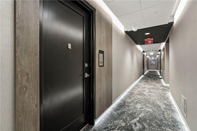 hallway featuring baseboards, a drop ceiling, visible vents, and attic access