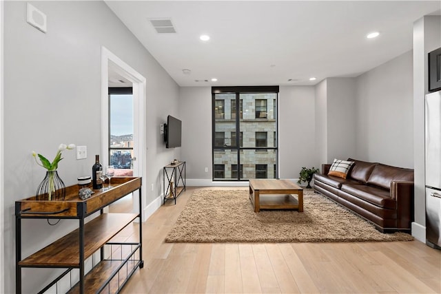 living area featuring baseboards, light wood finished floors, visible vents, and recessed lighting