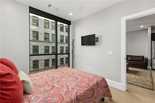 bedroom with wood finished floors, visible vents, baseboards, freestanding refrigerator, and floor to ceiling windows