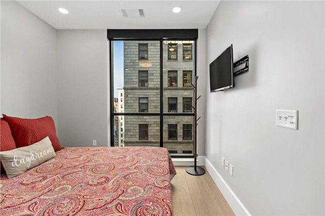 bedroom with a fireplace, visible vents, expansive windows, wood finished floors, and baseboards