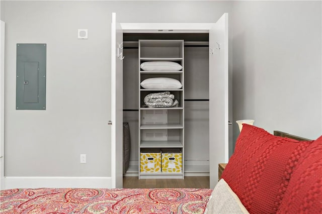 bedroom featuring wood finished floors, electric panel, and baseboards